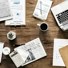 Biurko z laptopem, kalkulatorem, gazetą "Business" i notatkami. Idealne miejsce, by dowiedzieć się, jak napisać uzasadnienie.