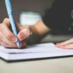 Dłoń pisze niebieskim długopisem w notatniku. Czy to chaos, czy haos?