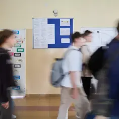 Rozmazani uczniowie idący szkolnym korytarzem obok tablic ogłoszeń.