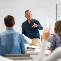 Nauczyciel matematyki tłumaczy zadania z geometrii uczniom w 3 klasie liceum. Na tablicy widać wzory i rysunki.