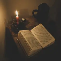 Światło świecy oświetla otwartą książkę, sugerując, jak literatura przedstawia kontrast między światem biedy a światem bogactwa.