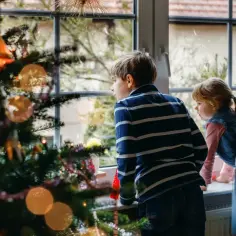 Dzieci patrzą przez okno, czekając, kiedy zaczyna się przerwa świąteczna. Choinka w tle.