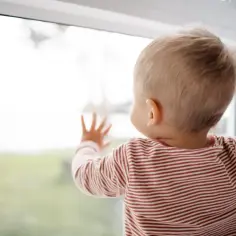 Małe dziecko w paski patrzy przez okno, zastanawiając się nad kolejnymi skokami rozwojowymi.