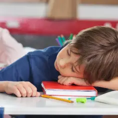 Chłopiec śpi na książce w szkole. Może to być jeden z powodów usprawiedliwienia nieobecności w szkole, gdy brakuje mu sił na naukę.