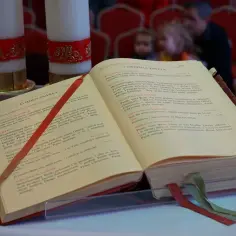 Otwarta księga liturgiczna z wstążkami, obok świec. Tekst zawiera modlitwy, w tym "mea culpa co to znaczy" - wyznanie winy.