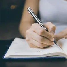 Dłoń pisze piórem w notatniku, planując, jak rozpocząć argument w rozprawce.