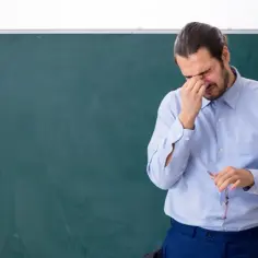 Nauczyciel z bólem głowy, trzymający okulary, zmęczony po całym dniu pracy. Dodatek za wychowawstwo chyba nie rekompensuje tego stresu.