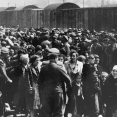 Tłum ludzi, w tym dzieci, zgromadzony przy wagonach kolejowych. Każdy człowiek zlagrowany jako ofiara zbrodniczego systemu, pozbawiony godności i nadziei.