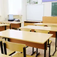Puste ławki i krzesła w klasie, gotowe na lekcję. Widać tablicę, projektor i komputer. Takie przedmioty są w siódmej klasie.