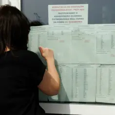 Kobieta sprawdza listę kandydatów, kiedy jest wystawienie ocen. Widać ogłoszenie o rekrutacji do przedszkola.