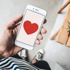 Dłoń trzyma smartfon z czerwonym sercem, symbolizującym co oznacza słowo love.