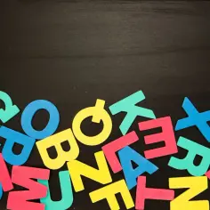 Kolorowe litery na czarnej tablicy, jakby ktoś uczył się, co to są głoski.