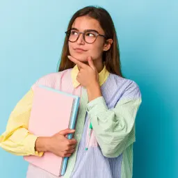 Młoda kobieta w okularach trzyma książki i zastanawia się, po jakich studiach jest praca.