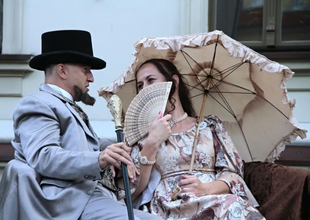 Elegancka arystokracja w lalce, mężczyzna w cylindrze i kobieta z wachlarzem pod parasolką, odtworzenie epoki.