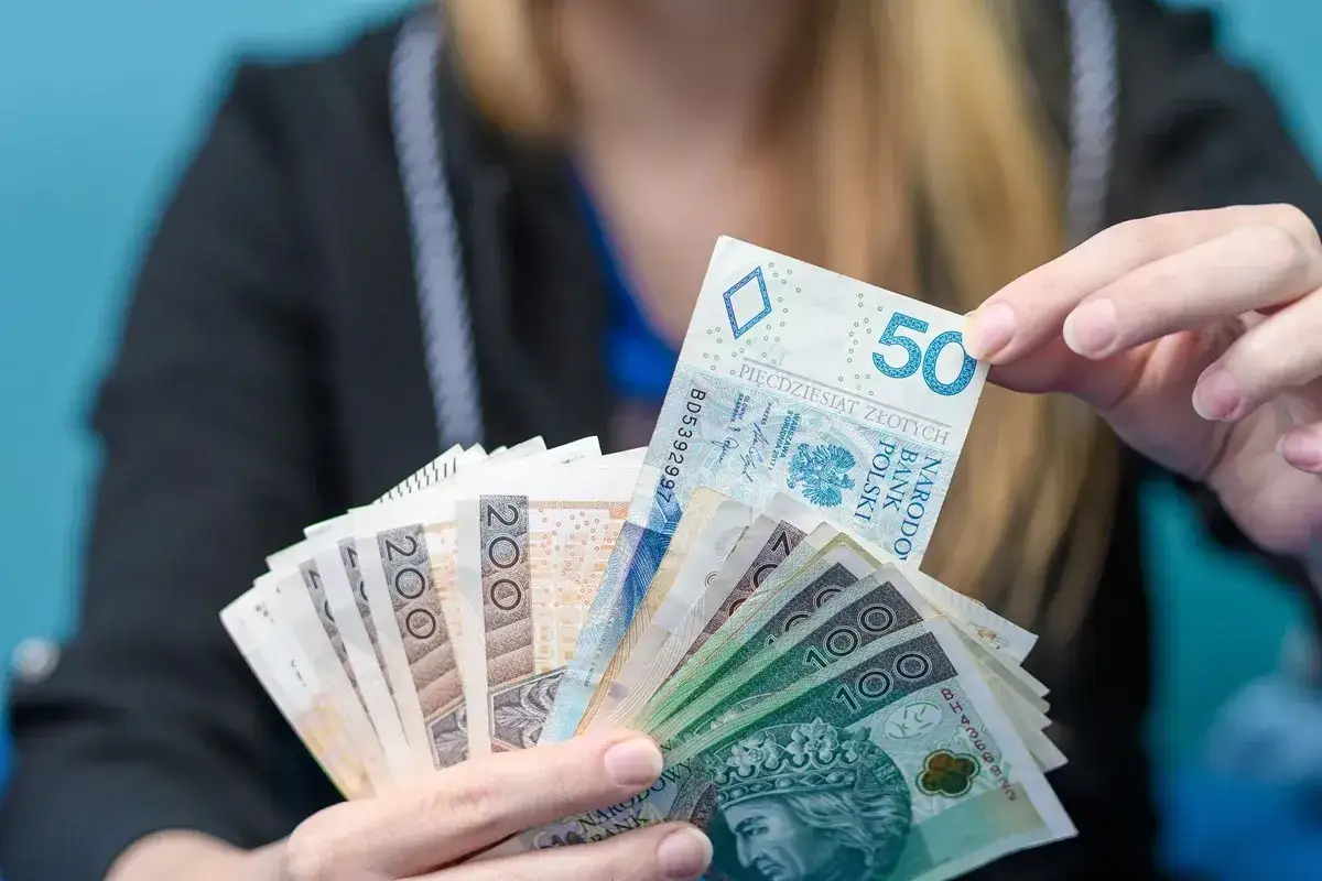 Ręce trzymające polskie banknoty, symbolizujące świadczenie na start dla nauczycieli. Widać nominały 50, 100 i 200 zł.