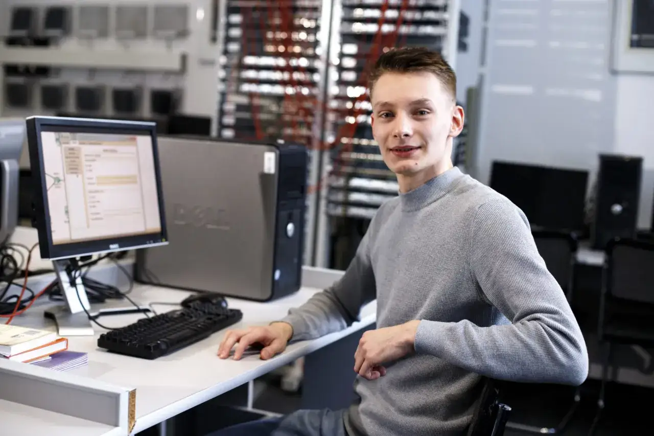 Młody informatyk przy biurku z komputerem. Zastanawiasz się, ile zarabia informatyk po studiach?