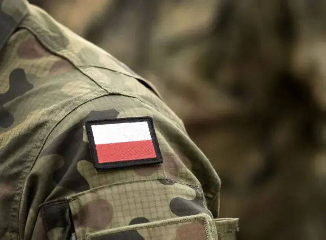 Żołnierz w mundurze moro z naszywką z polską flagą. Po studiach wojskowych zdobywa swój pierwszy stopień wojskowy.